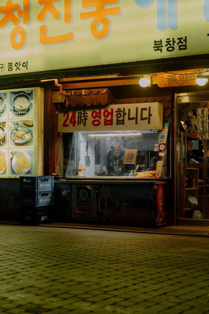 A charming Korean street food stall operating 24/7, illuminated at night in an urban setting.