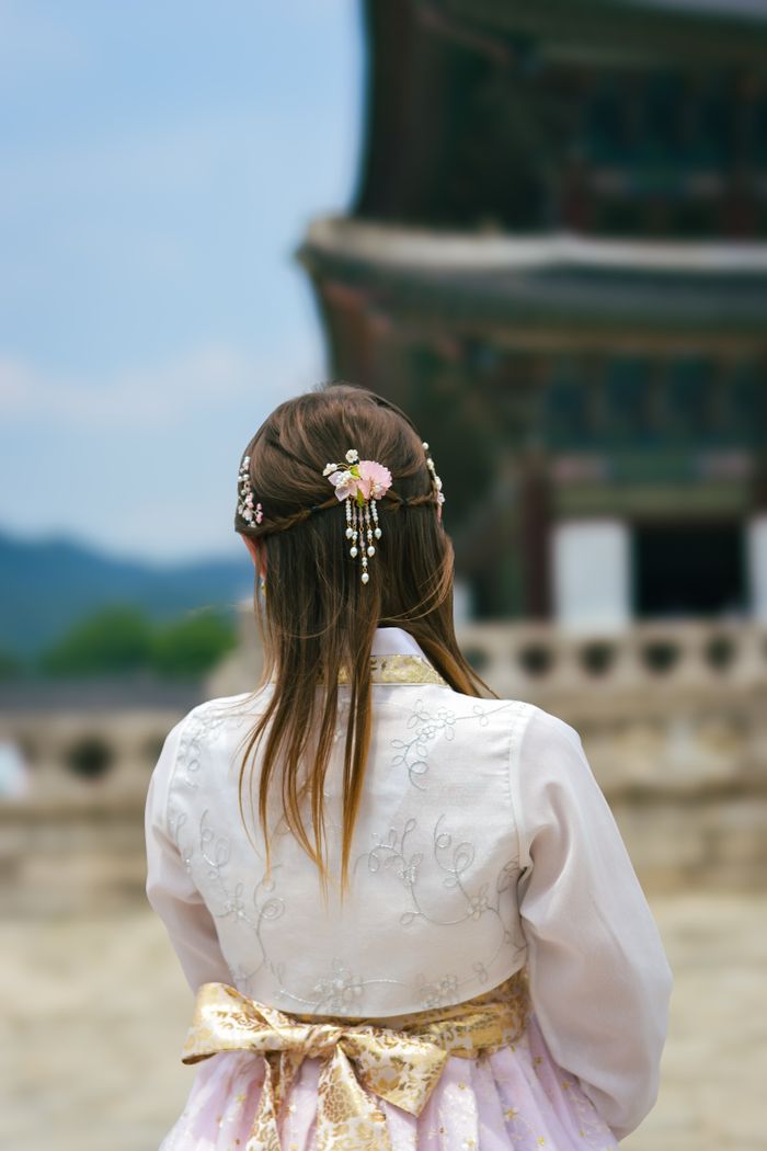 A woman in a hanbok admires the architecture of a South Korean palace.