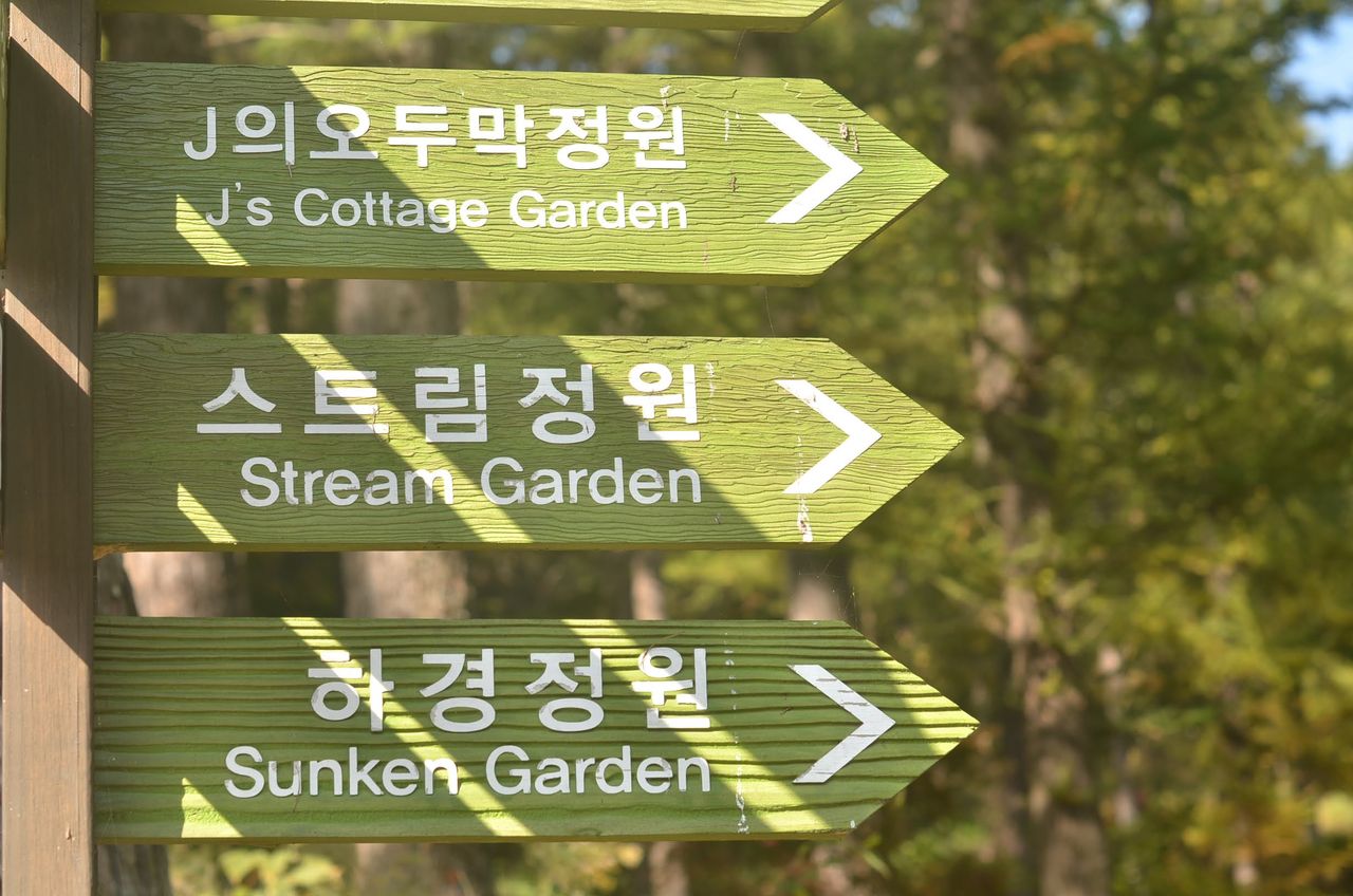 Directional signs point to different gardens in a tranquil Korean setting.